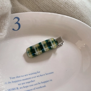 Detail view of a green plaid acetate hair clip on a decorative ceramic plate with knit background