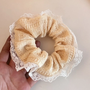 Close-up of beige knit hair scrunchie featuring delicate white lace trim detail