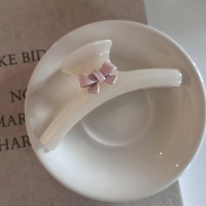 Creamy white hair claw clip with a 3D pink bow accent resting in a white porcelain bowl