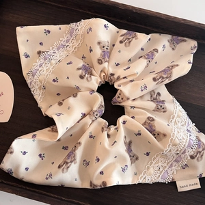 Vue détaillée d'un chouchou crème avec motif d'ours et bordure en dentelle blanche