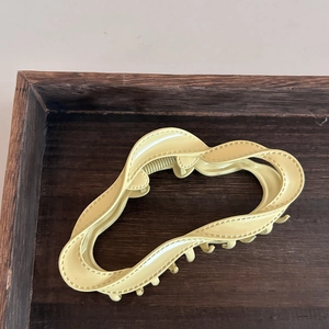 Pince à cheveux crème en forme de nuage avec texture ondulée sur plateau en bois