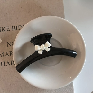 Detail of a large black claw clip with white 3D bow design on a ceramic plate