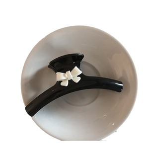Elegant large black hair claw clip with white bow accent on a white ceramic plate