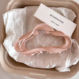 Détail d'une pince à cheveux nuage rose ondulée mate présentée sur un plateau
