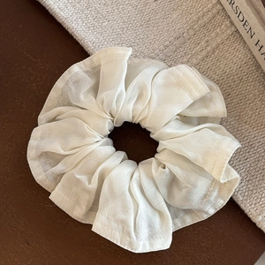 Détail d'un chouchou en satin crème élégant montrant la texture plissée sur bois