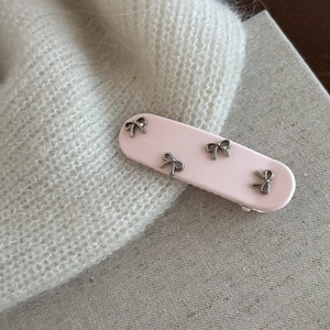 Dettaglio del fermaglio rosa ovale con quattro decorazioni metalliche a fiocco