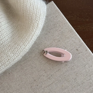 Dettaglio del fermaglio rosa ovale con un piccolo fiocco d'argento su fondo grigio