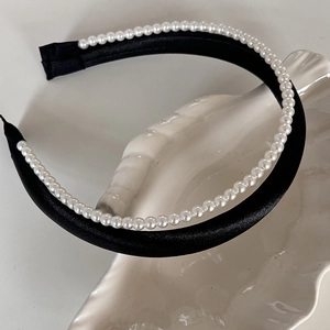 Détail de perles blanches sur serre-tête en soie noire posé sur plateau coquillage