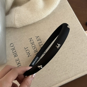 Dettaglio di un cerchietto nero spesso con fiocchi in metallo argento su un libro beige