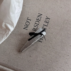 Elegant silver glitter hair clip with a black ribbon bow on a minimalist textured background