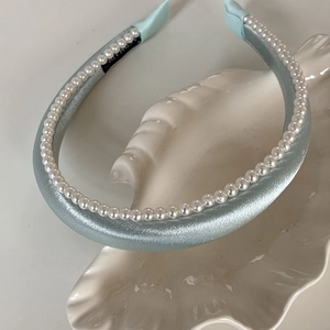 Détail du serre-tête en satin bleu clair avec perles sur un plateau en nacre
