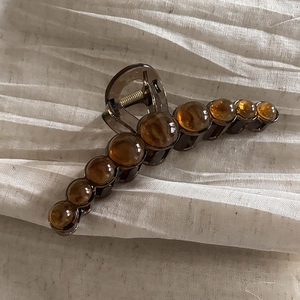 Large amber acrylic hair claw clip with pearl beads on white textured linen fabric