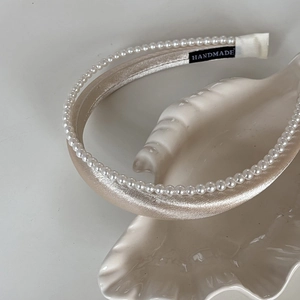 Détail du serre-tête en satin champagne avec perles blanches et étiquette faite main