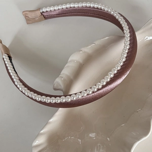 Vue détaillée d'un serre-tête en satin rose avec perles blanches sur un plat