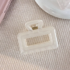 Détail d'une pince à cheveux rectangulaire ajourée blanc crème sur fond texturé élégant