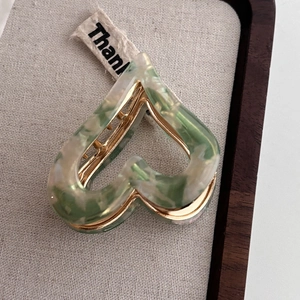 Detail of heart-shaped acetate hair claw with green marble texture and golden metal spring