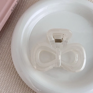 Pince à cheveux nœud blanc crème sur assiette blanche pour coiffure élégante et minimaliste