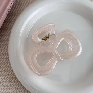 Pince à cheveux papillon rose crème en résine sur un plateau en céramique blanche
