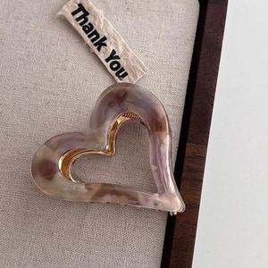 Close-up of heart-shaped acetate claw clip with marble texture and gold metal teeth