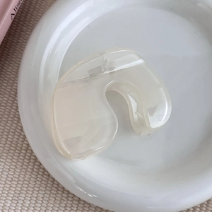 Gros plan d'une pince à cheveux en forme de U blanc crème sur un plateau en céramique