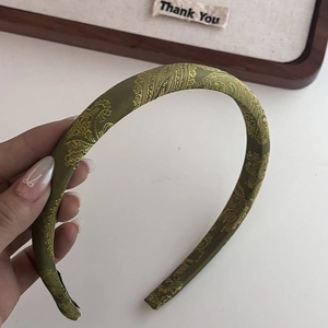 Détail d'un serre-tête en soie vert foncé avec motif Paisley doré et texture élégante