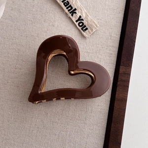 Close-up of deep brown acetate heart hair claw with golden metal teeth and glossy finish