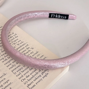 Elegante cerchietto imbottito in raso rosa perlato appoggiato su un libro aperto