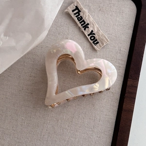 Detail of a pearlescent ivory acetate heart claw clip with golden metal springs and teeth