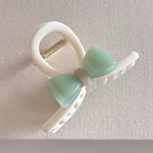 Detail of mint green acetate bow hair claw clip with golden metal spring and cream resin base