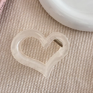 Gros plan d'une pince à cheveux en forme de cœur blanc crème sur un tapis tissé