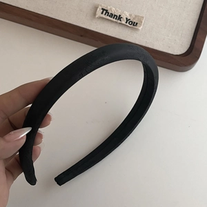 Détail d'un serre-tête vintage en tissu noir texturé sur un plateau en bois