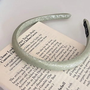Dettaglio di un cerchietto plissettato verde menta appoggiato su un libro d'epoca aperto