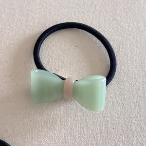 Detailed view of mint green jelly bow hair tie on a rustic cream fabric background