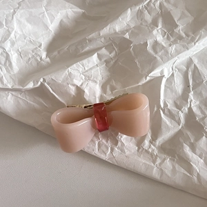 Detail of pink acetate bow hair clip with red center on white textured background