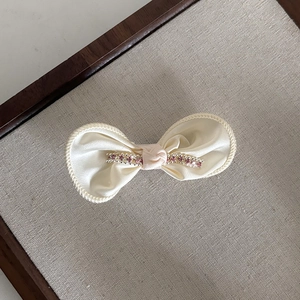 Barrette nœud papillon crème avec cristaux roses sur fond de textile texturé
