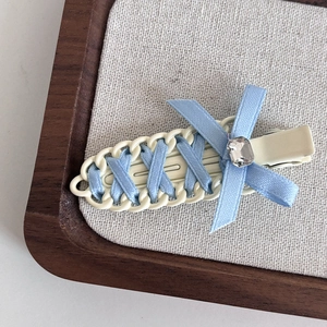 Light blue ribbon bow hair clip with crystal accent on cream woven seamless base