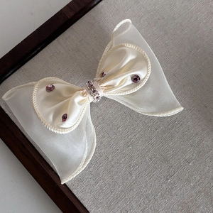 Détail de la barrette à cheveux en organza crème avec strass violets et satin