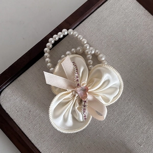Détail d'un nœud en satin crème avec cœur en strass rose et chaîne de perles