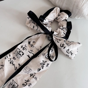 Close-up of beige ink-style scrunchie with calligraphy ribbons and gray translucent beads