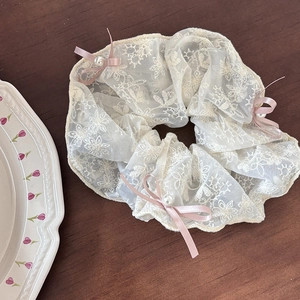 Detaillierte Nahaufnahme von cremefarbenem Spitzen-Scrunchie mit rosa Schleifen und Perlen