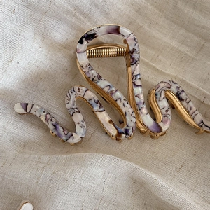 Elegant gold-tone S-shaped hair claw with purple marble resin inlay on linen background