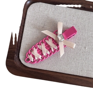 Pink carrot-shaped hair clip with woven beige ribbons and a sparkling rhinestone bow