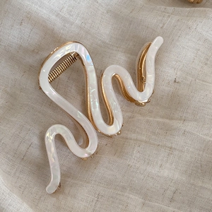 Detail view of wave-shaped cream hair claw clip with golden metal base on beige linen
