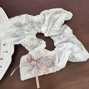 Detail eines Spitzen-Haargummis mit rosa Satinschleife und Perlen auf Holz