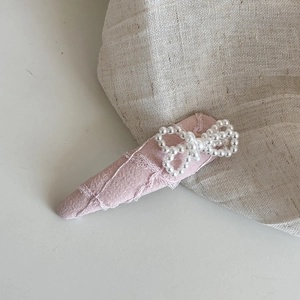 Détail d'une pince à cheveux rose en tissu avec nœud en perles et bord en dentelle