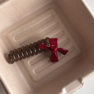 Brown spiral hair tie with red glossy ribbon bow on minimalist beige fiber tray