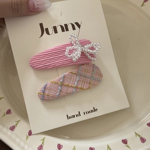 Detailed close-up of pink tweed and corduroy hair clips with pearl bow on display card