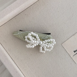 Barrette en dentelle verte avec nœud en perles blanches sur plateau en lin