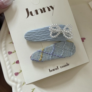 Detailed macro of two light blue plaid hair clips with pearl bow on white display card