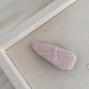 Détail d'une pince à cheveux en jacquard rose avec motifs de dentelle blanche sur lin